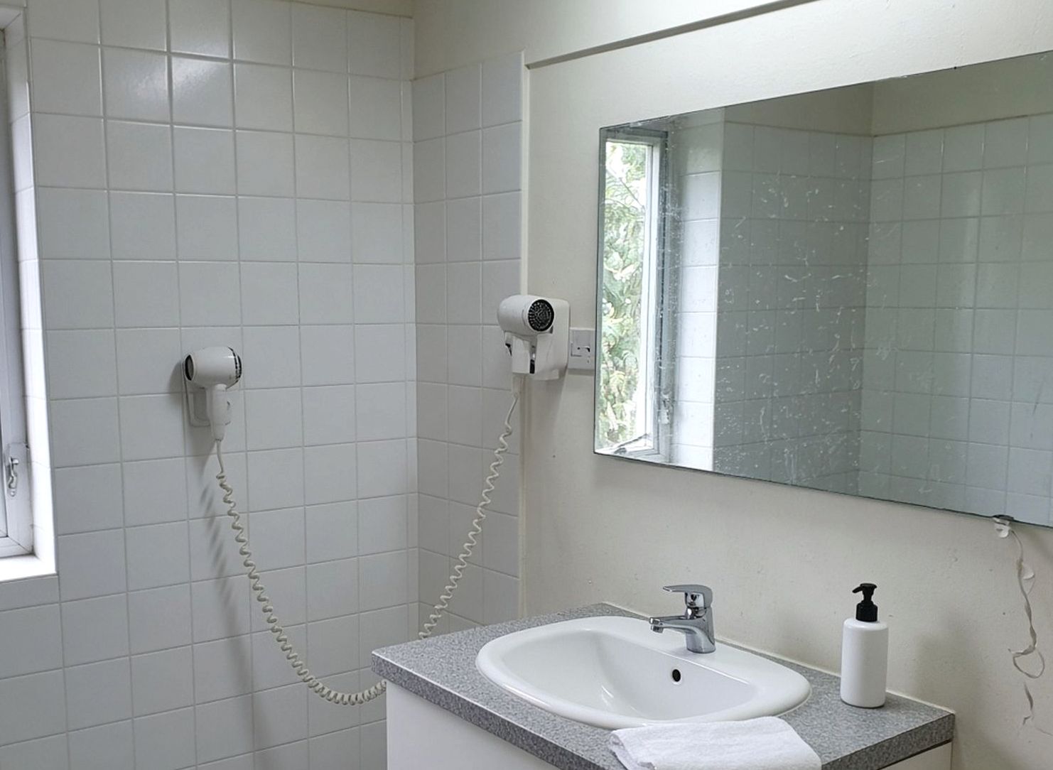 Small hotel bathroom with white tiles and a spotted mirror