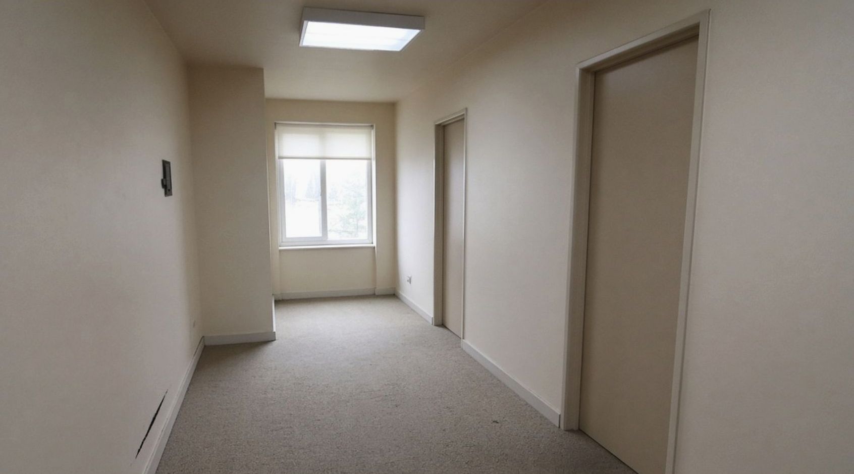 Short hotel corridor with blank doors and a window at the far end