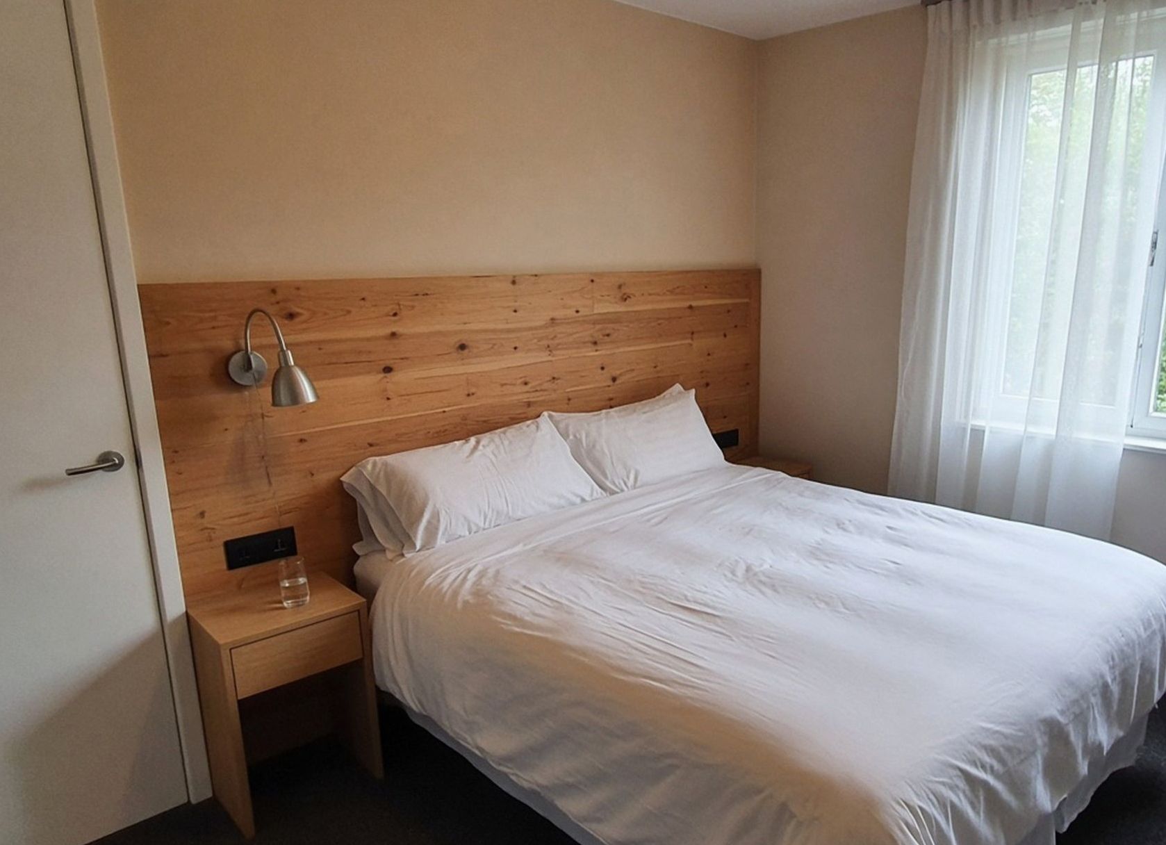 Queen bed with a timber headboard and a wall lamp in a Glen Eden hotel room