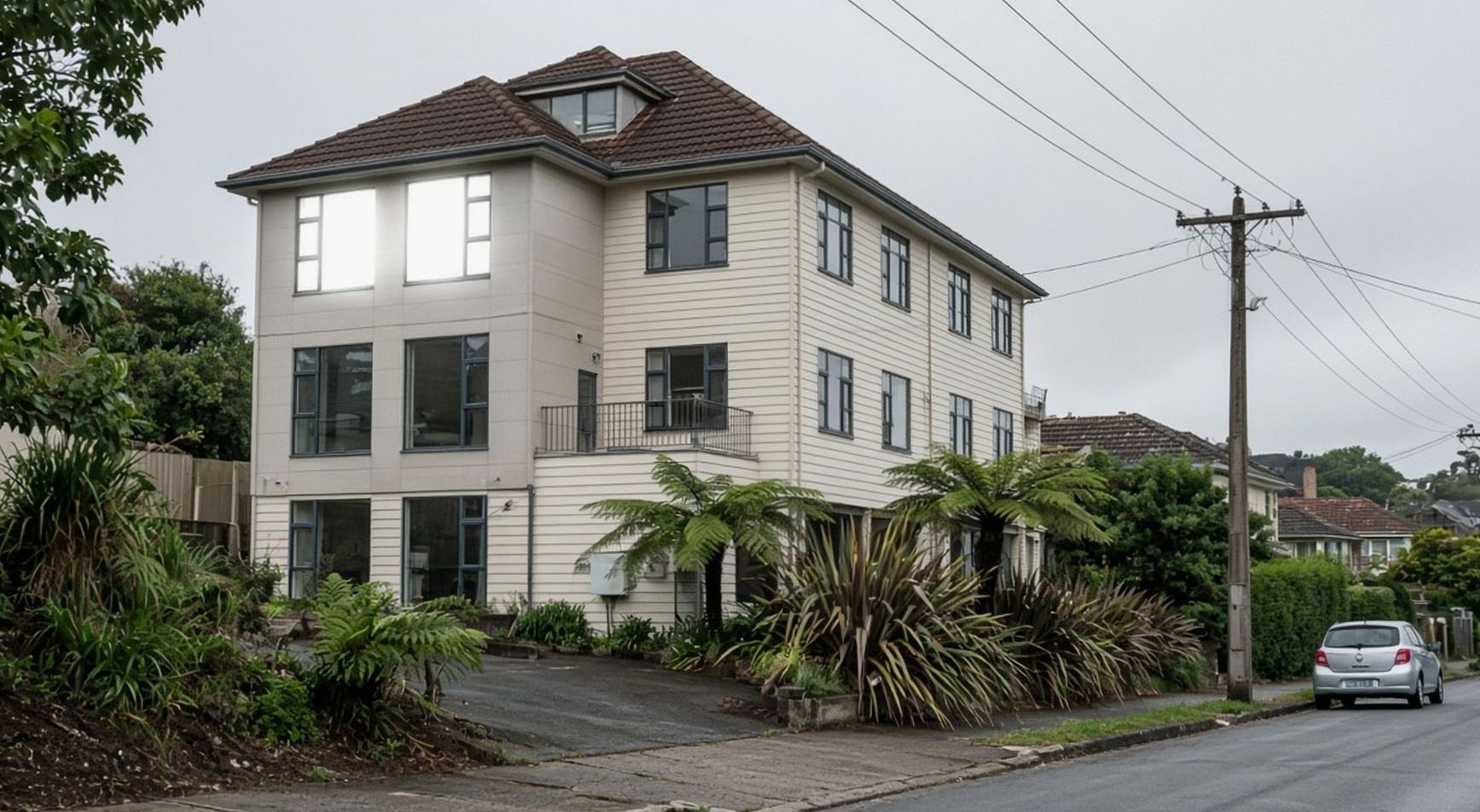 Three-storey cream hotel with flax and a parked hatchback on Wilson Road