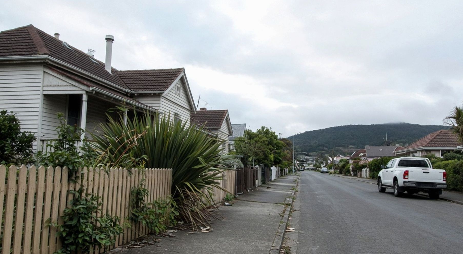 Wilson Road looking west past weatherboard houses toward the Waitākere hills